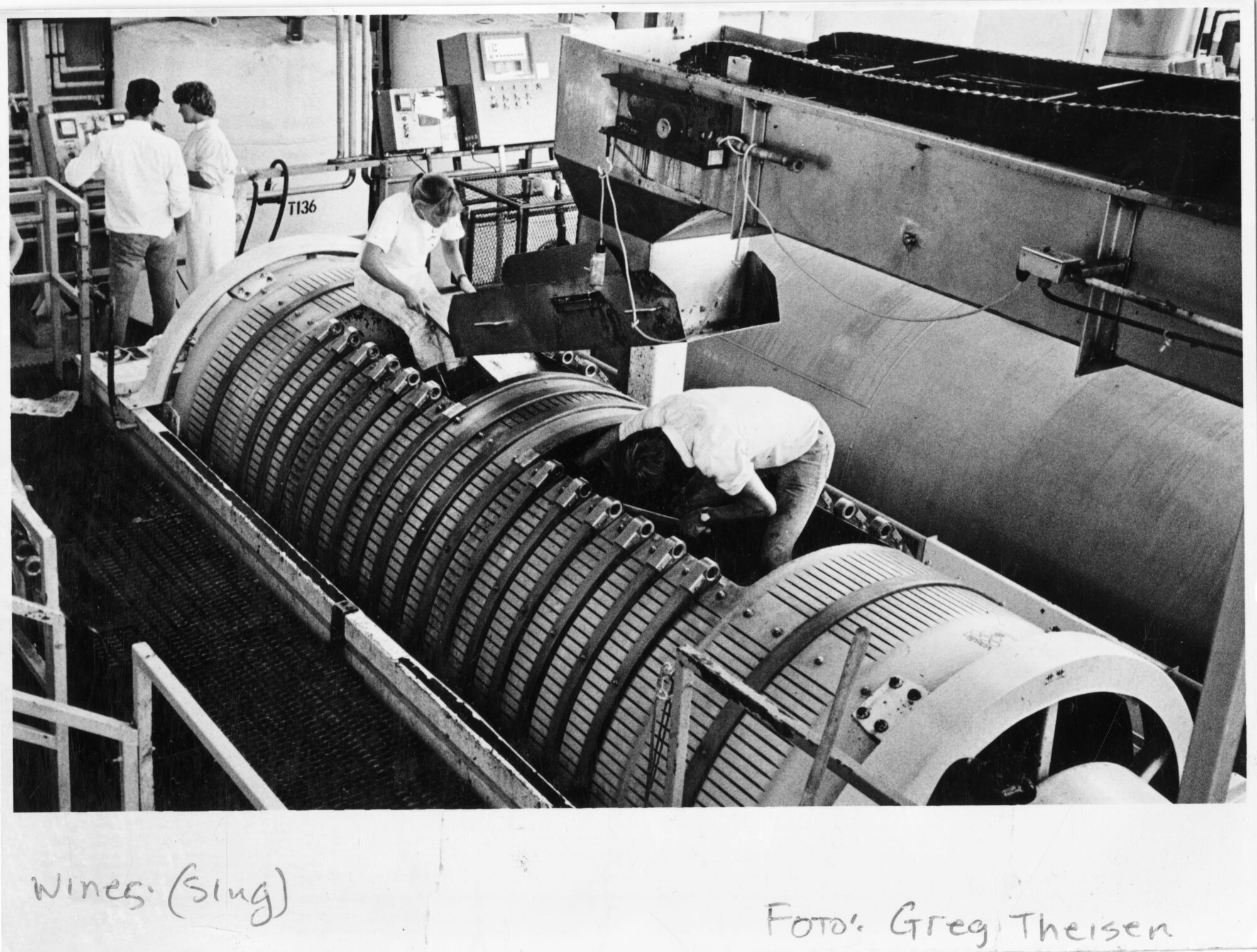 Four workers actively working on an industrial wine press at Christian Brothers Winery
