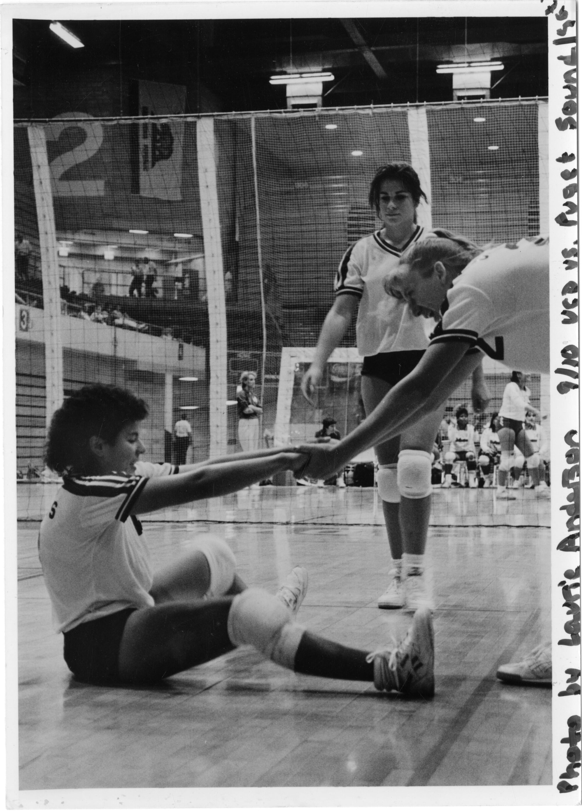 Volleyball player laughing while helping a teammate stand up from the floor