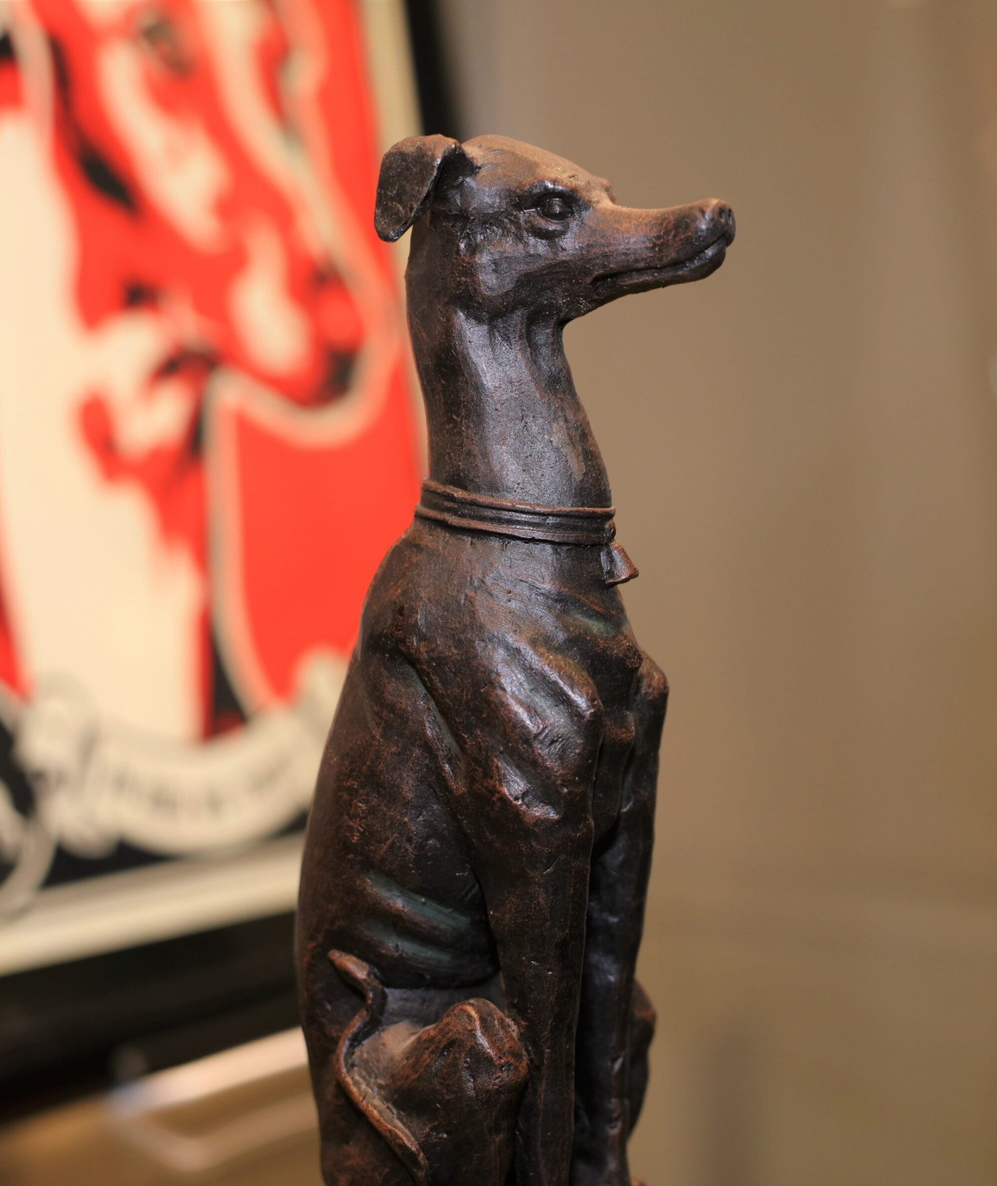 Sculpture of a sitting greyhound in profile looking vigilant.