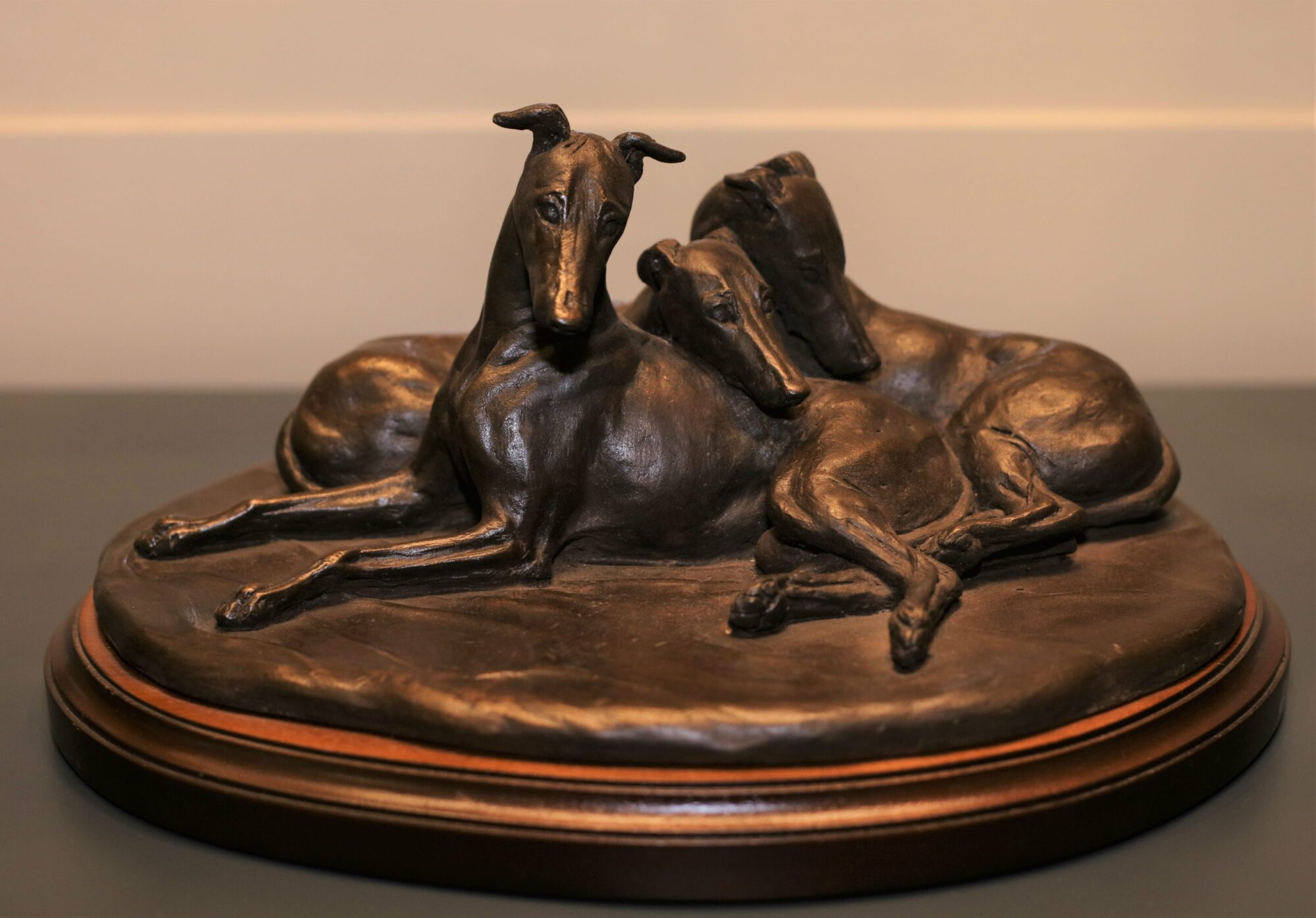 Sculpture of three greyhounds cuddling together on a low pedestal.