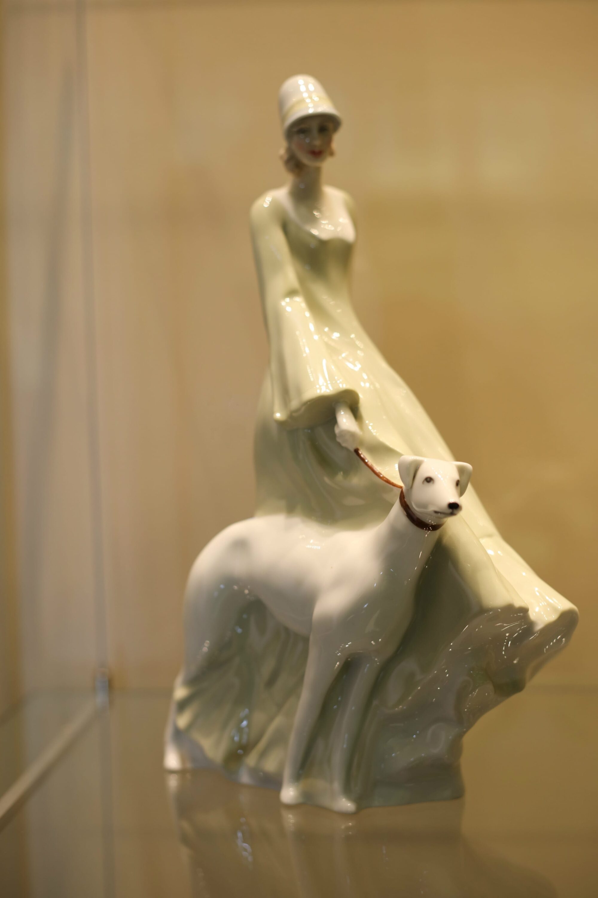 Ceramic of a woman wearing 1920s style clothing walking a white greyhound.