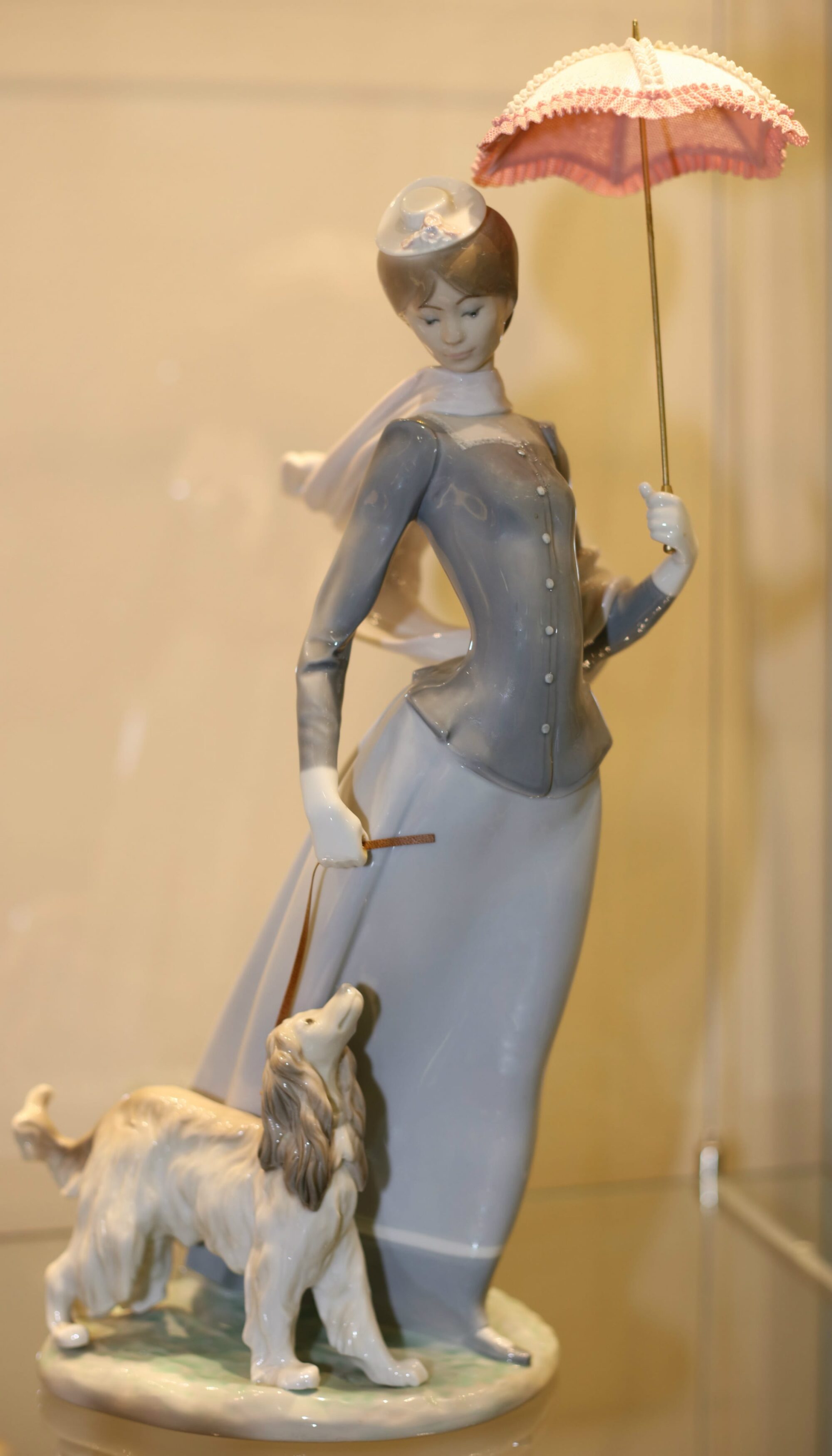 Ceramic of a woman in turn of the century clothing holding a parasol and walking a petite Afghan hound.
