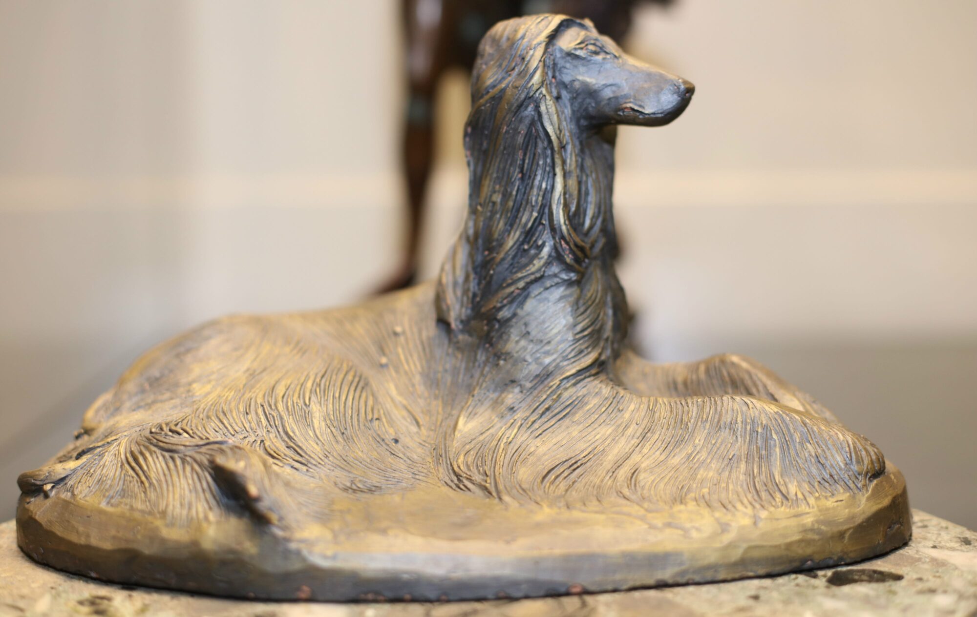 A slightly abstract sculpture of a sitting Afghan hound with its long fur fading into the base.