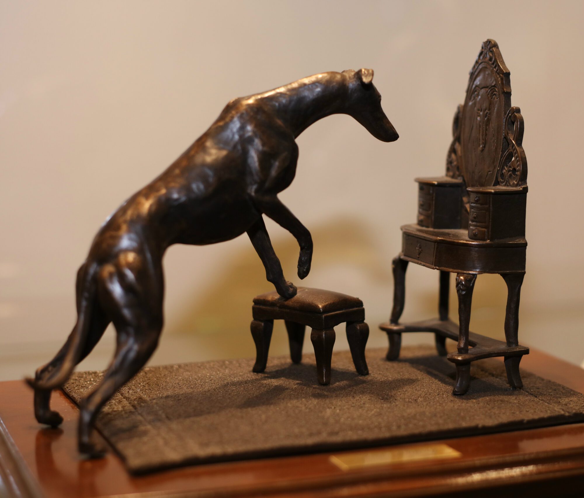 Sculpture of a greyhound stepping on a stool to look into a vanity mirror.