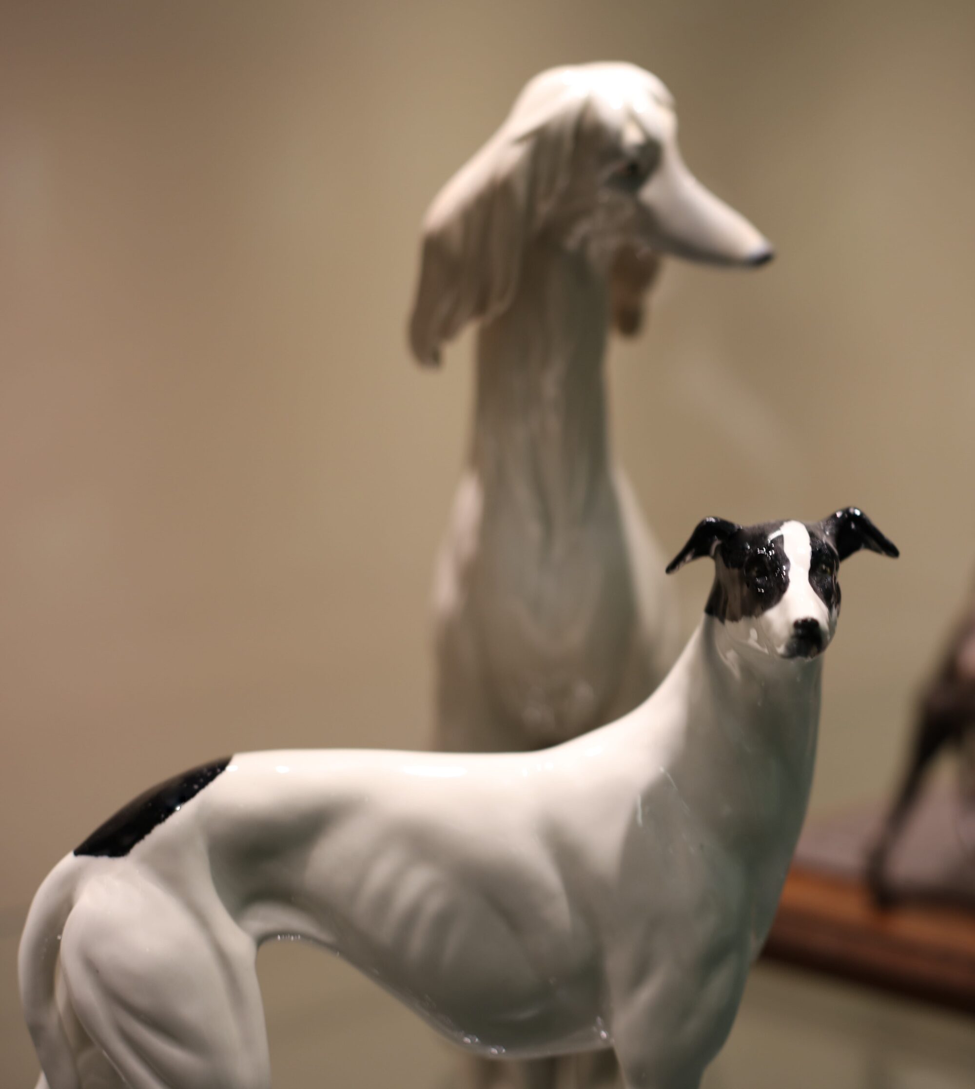A standing white ceramic greyhound is in the foreground with a taller, sitting ceramic Afghan hound in the background.