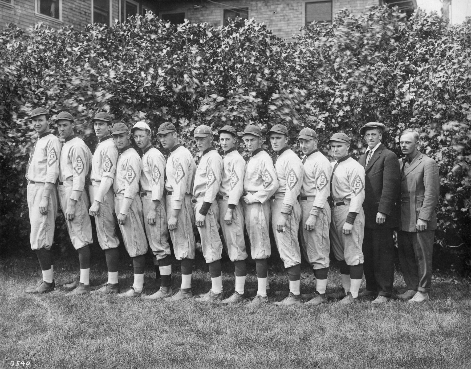 12 men in uniform and two in suits standing in a single file line