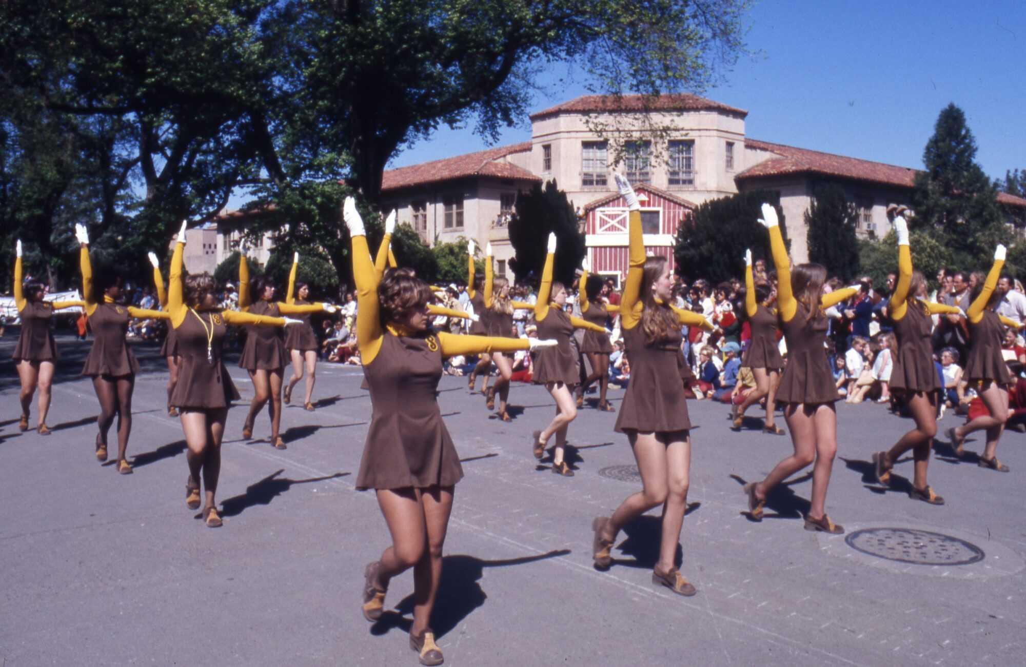 Women wearing matching brown dresses with yellow sleeves performing a routine in the parade