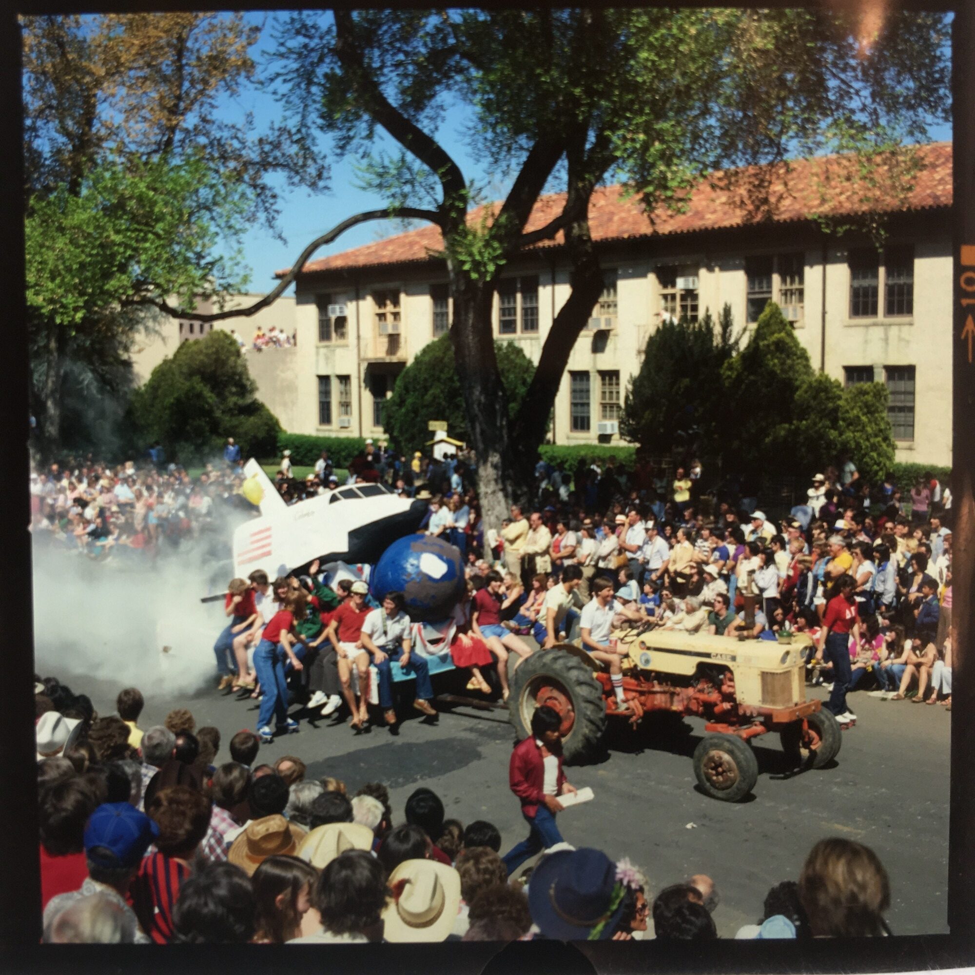 Tractor pulling a space shuttle float with lots of onlookers