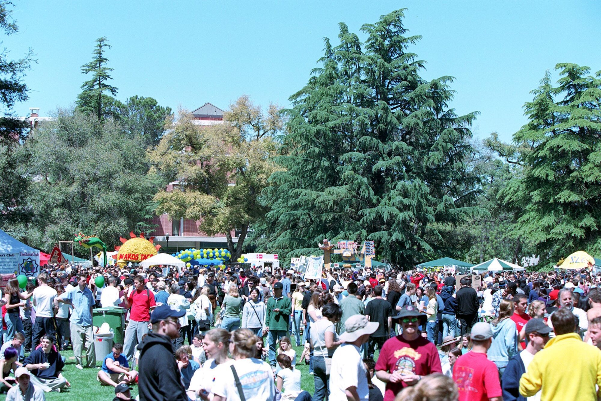 A large crowd of students and visitors relaxing on the grass and browsing booths