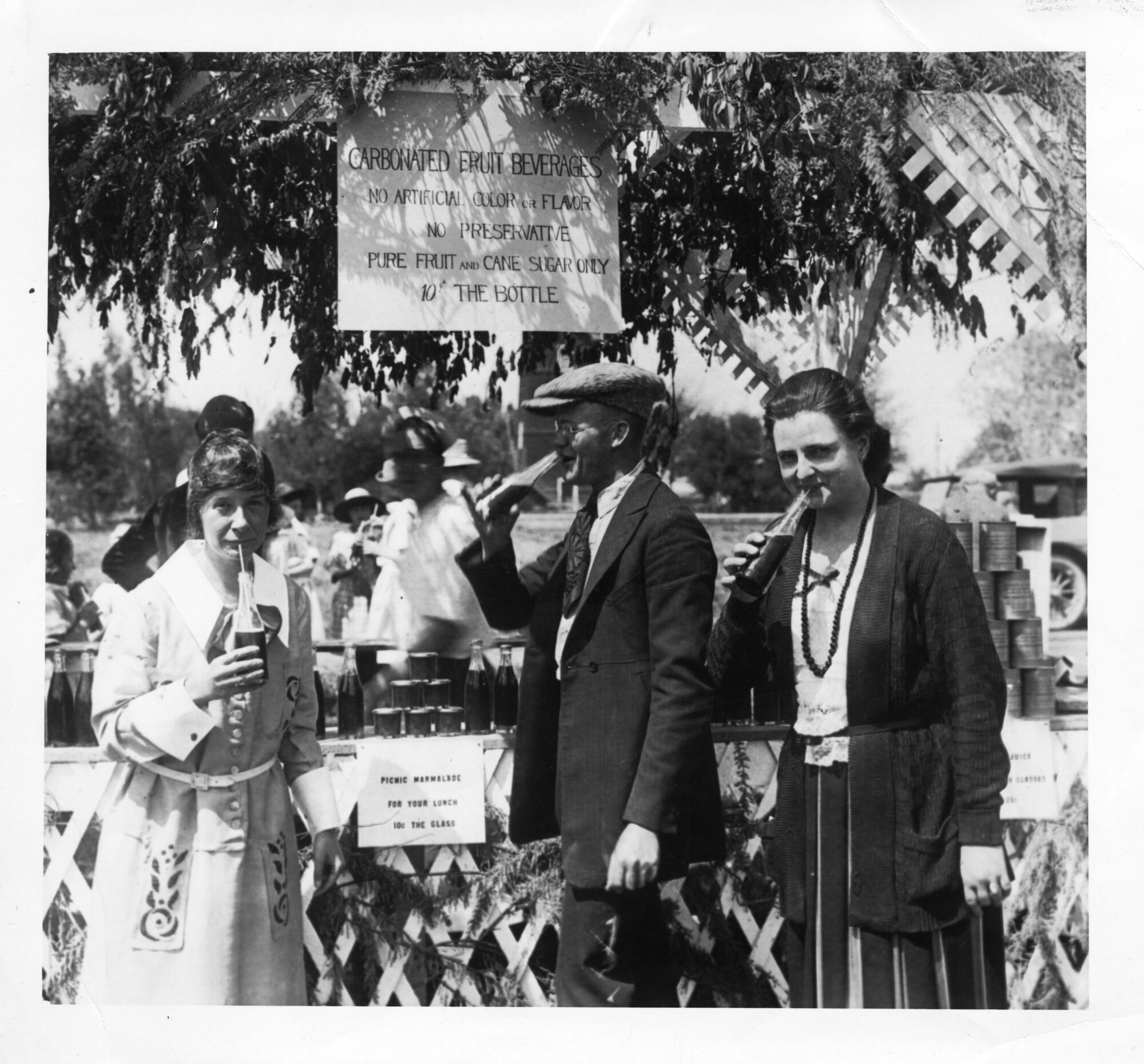 Two women and a man drinking carbonated fruit beverages from bottles