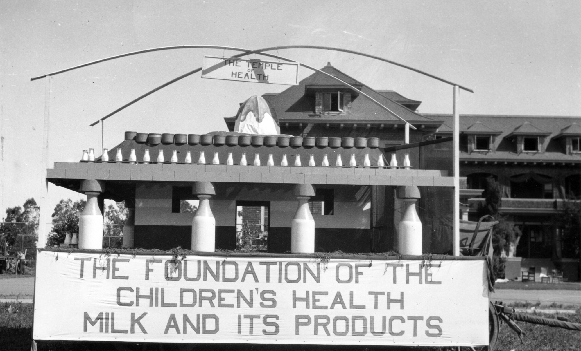 Float with pillars of milk bottles holding up rows of smaller milk bottles with sign reading: the foundation of the children's health milk and its products