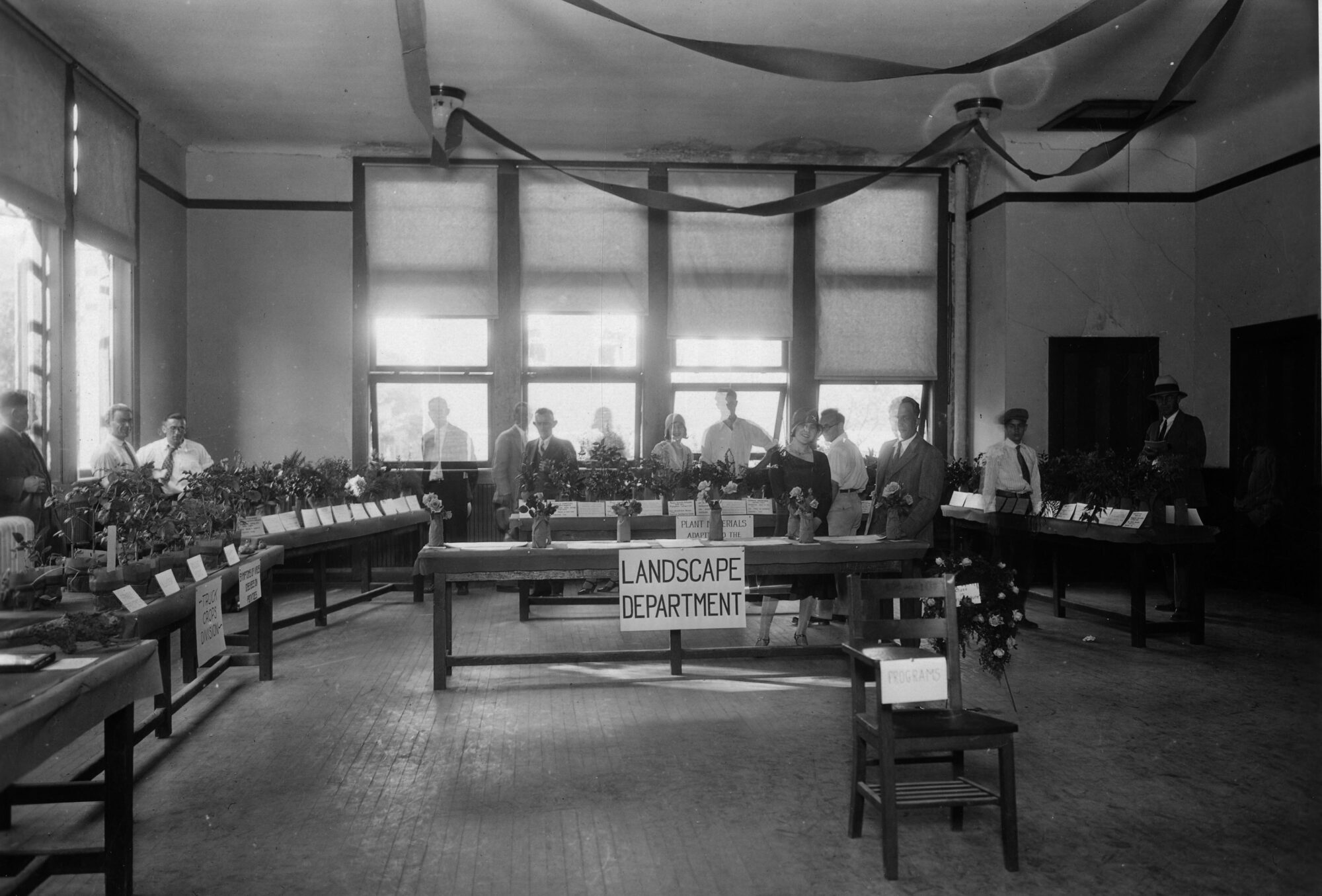 People standing behind plant-filled tables lining a room