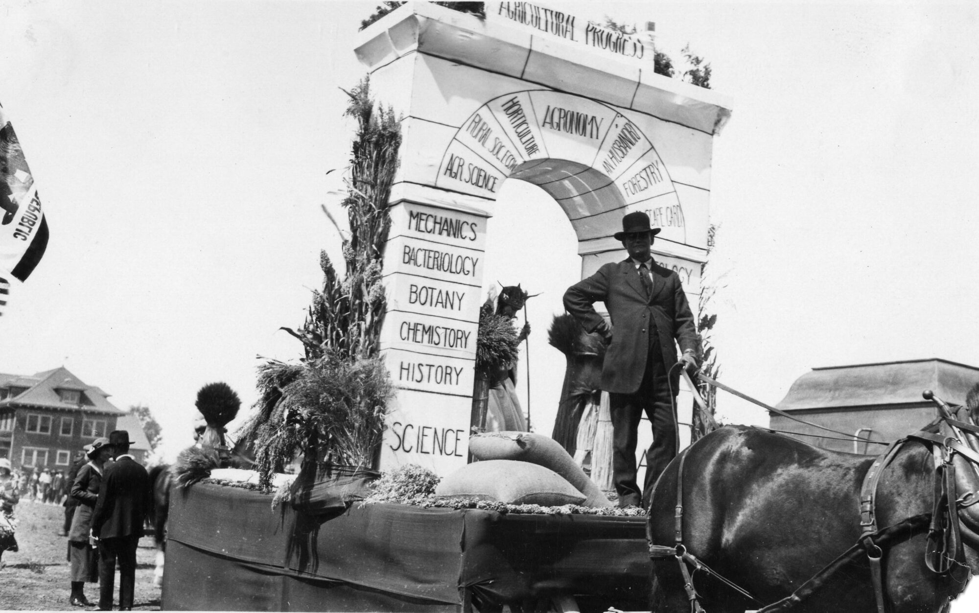Horse pulling an arch shaped float featuring key areas of agricultural progress such as science, history, chemistry, botany, mechanics, and more