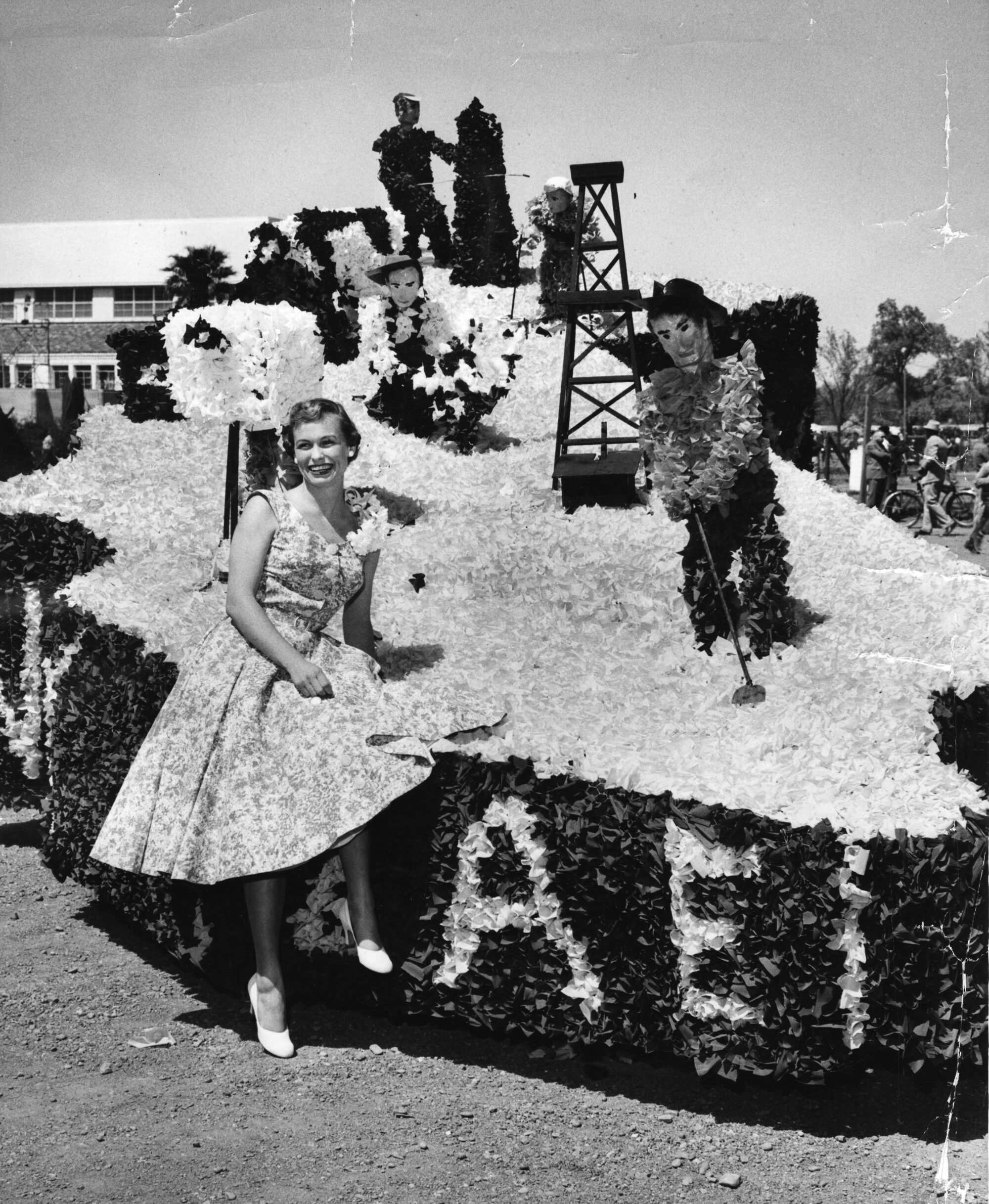 Woman sits on front of float of paper people doing agricultural work