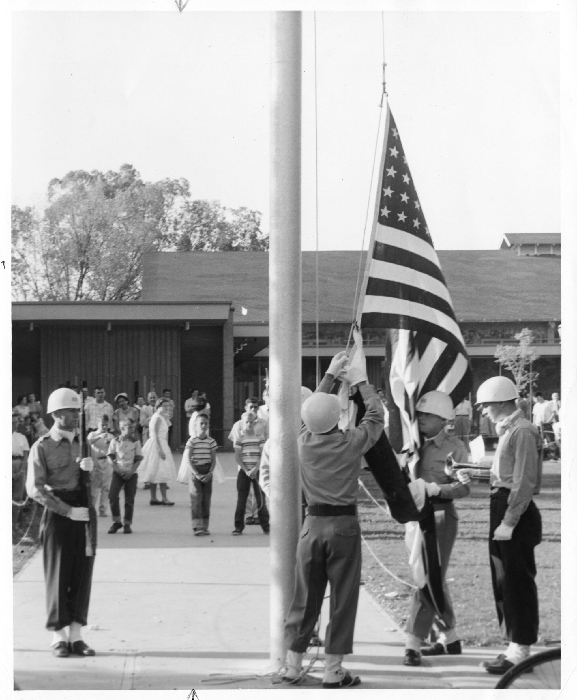 Two men raising an American flag flanked by a man with trumpet and a man with a rifle