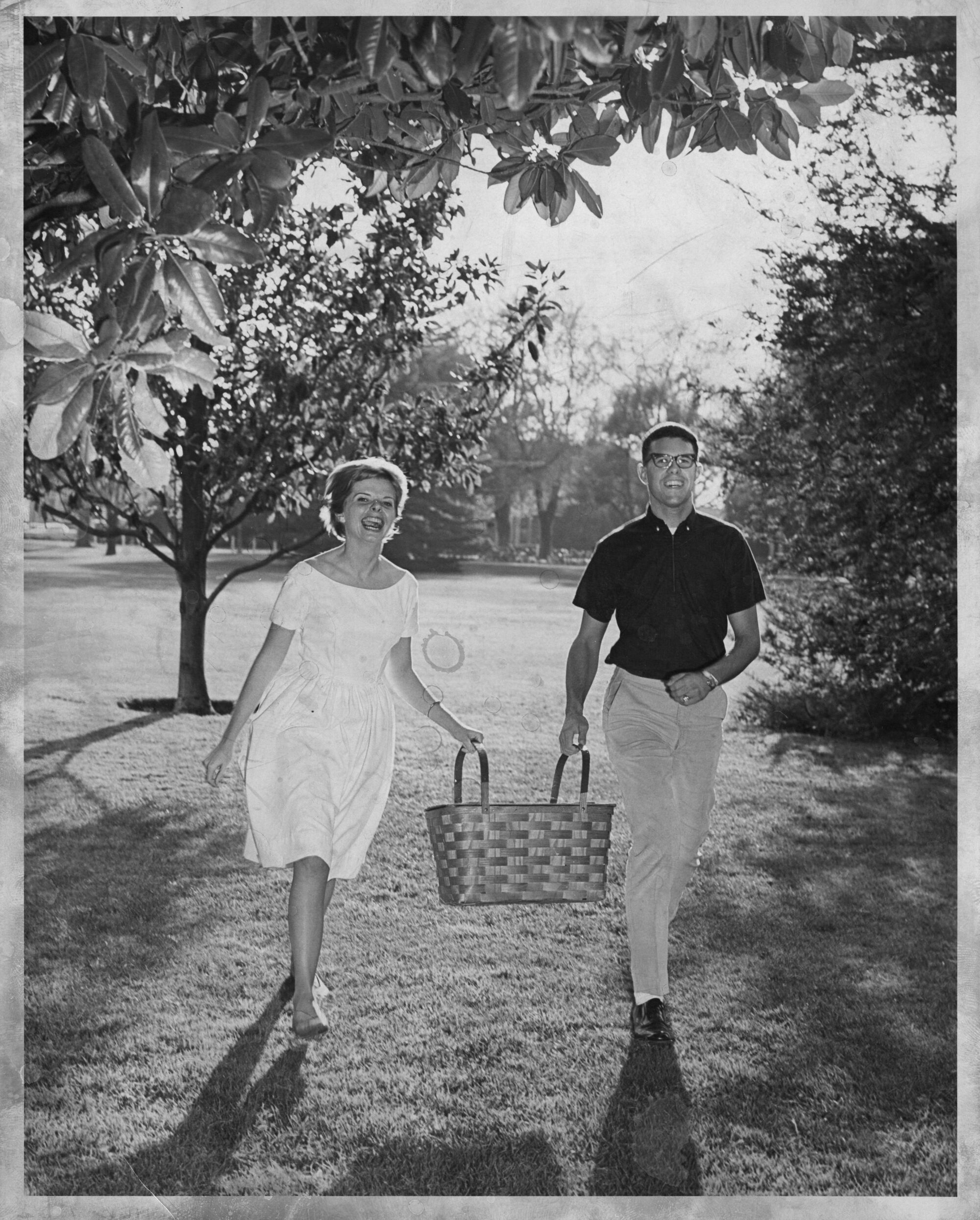 Smiling man and woman walking while holding picnic basket between them