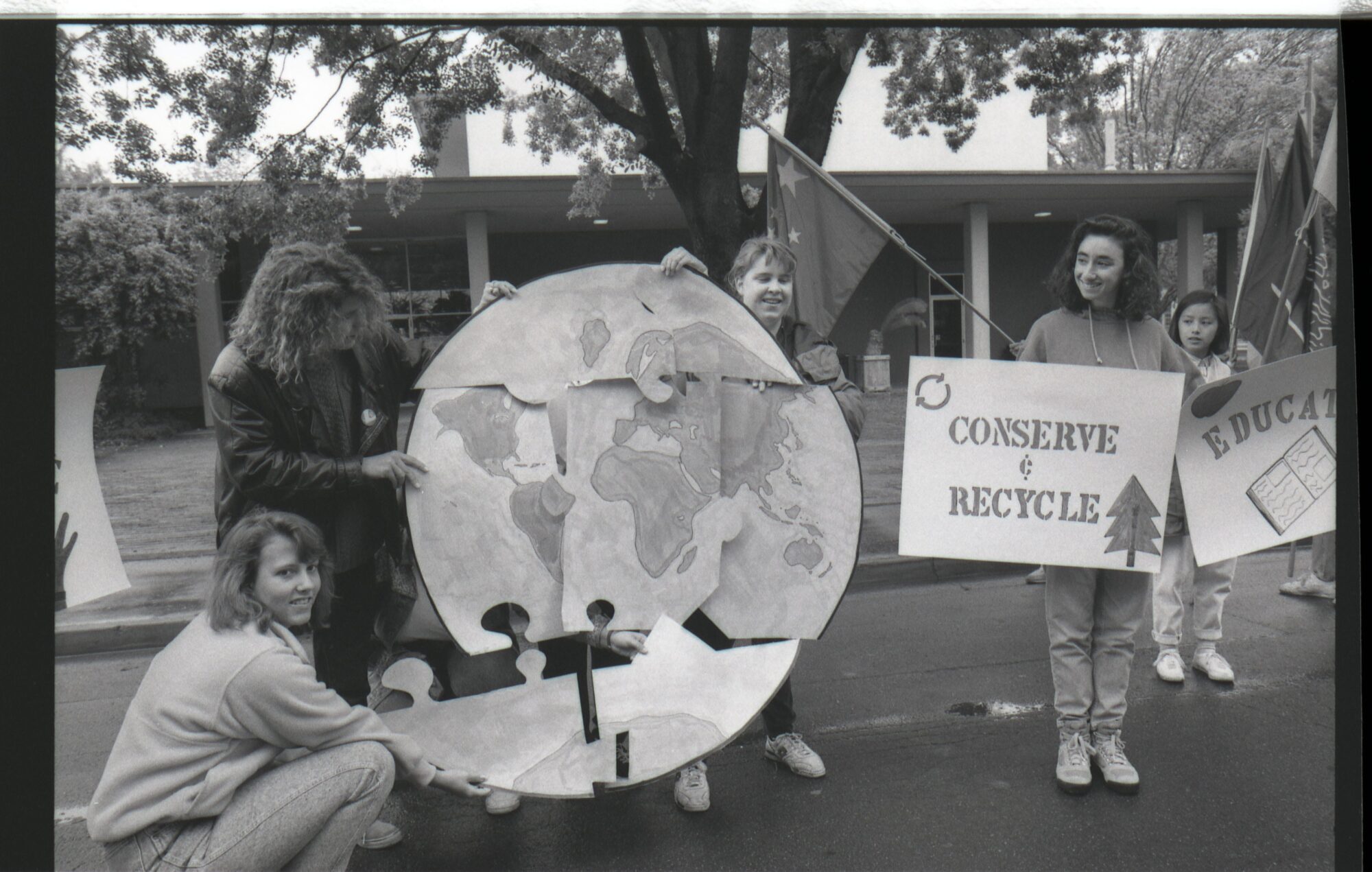 Students holding giant puzzle pieces of earth together with a "Conserve and Recycle" sign