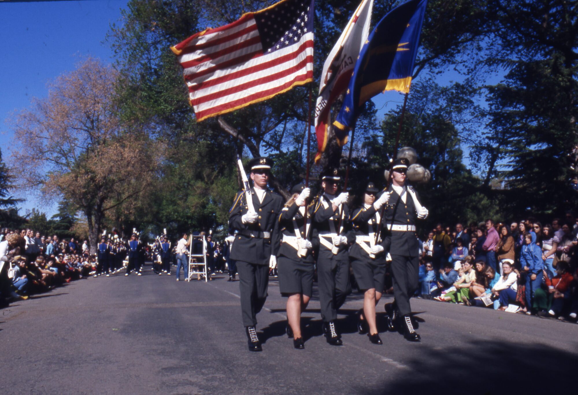 Five ROTC members carrying a rifle, American flag, California state flag, and blue regimental color flag