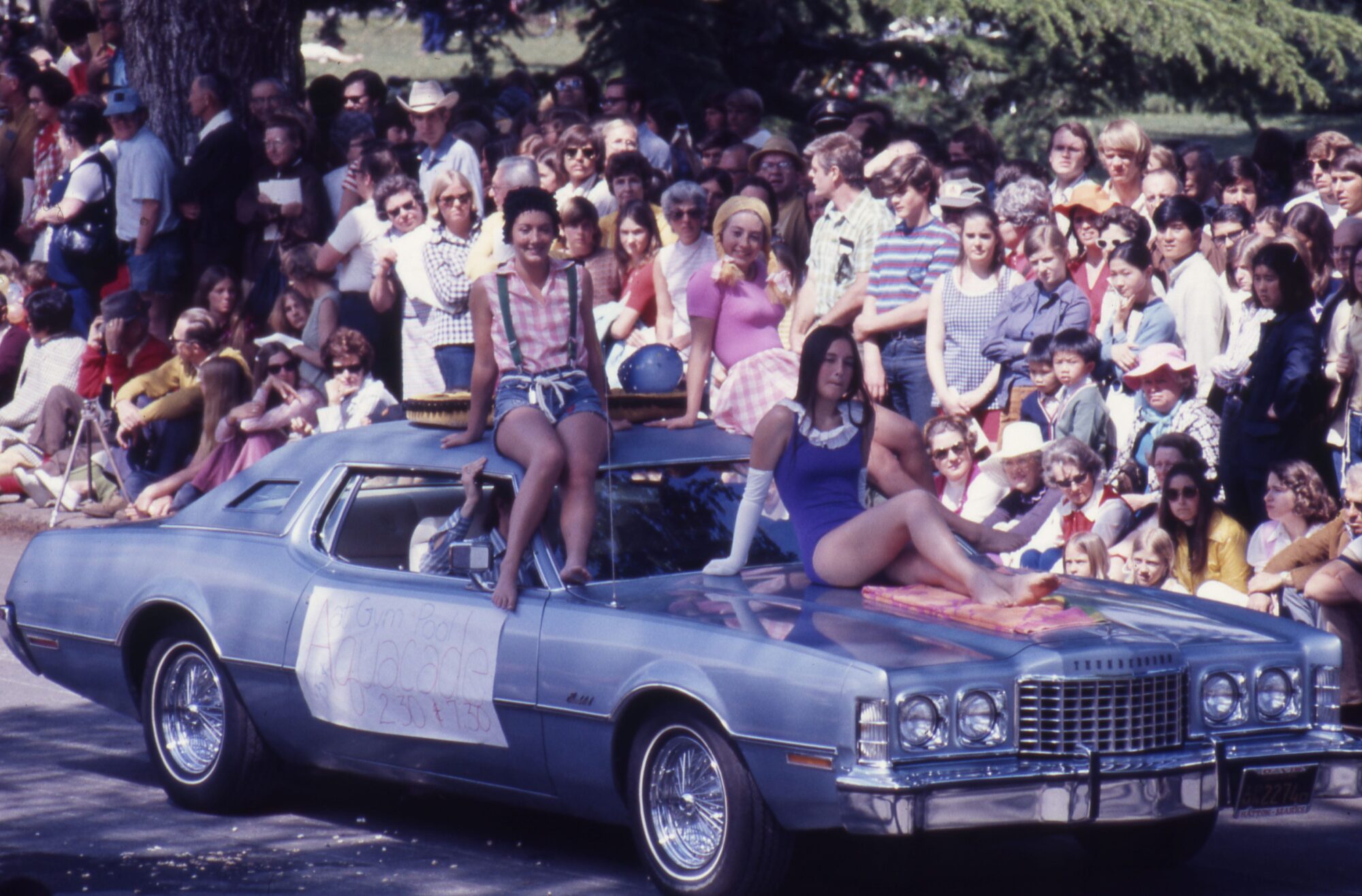 Women in summer attire sitting on the hood of a car