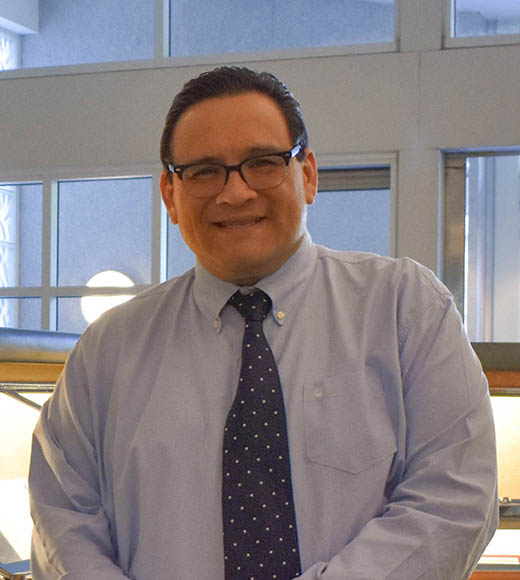 Smiling man with short dark hair wearing glasses and a tie