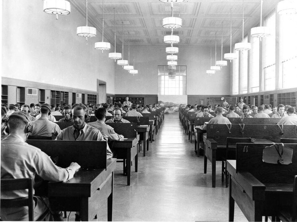 Army Signal Corps trainees wearing headsets work at rows of tables in Shields Library Main Reading Room during World War Two