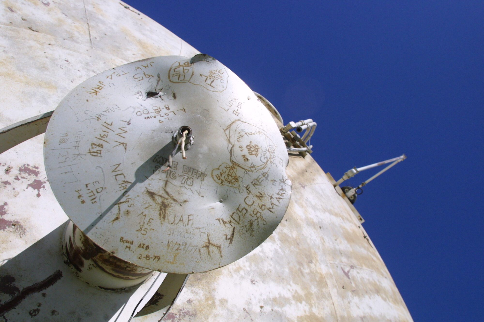 The top of a fallen water tower covered in graffiti scratched onto beacon cover, including Mike Duffy 3-16-78 and TL 95.