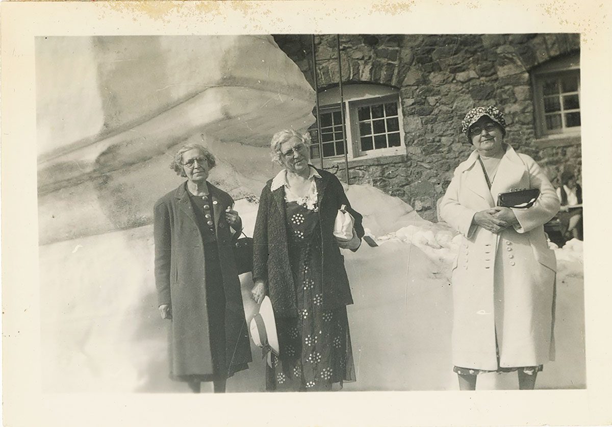Three women standing in front of a stone building.