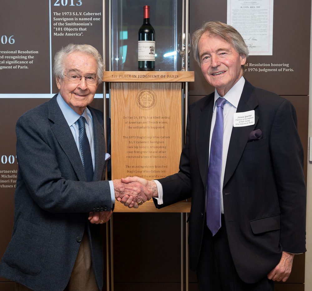 Warren and Steven shaking hands in front of the "1st place judgement of Paris" exhibition display, including a bottle of the winning wine.