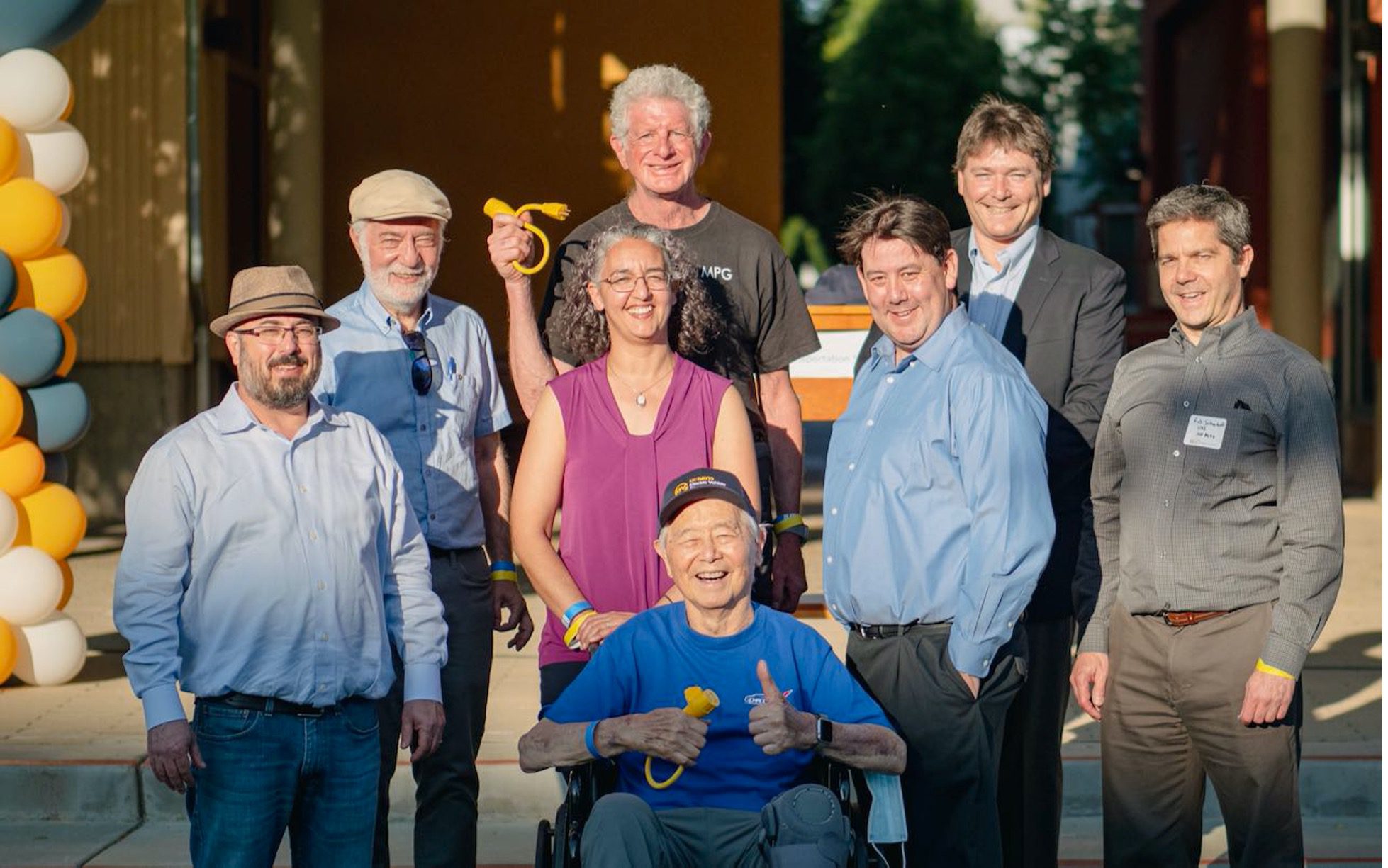 A group of people standing outside for a group photo. Two people are holding yellow electrical cords as they pose.