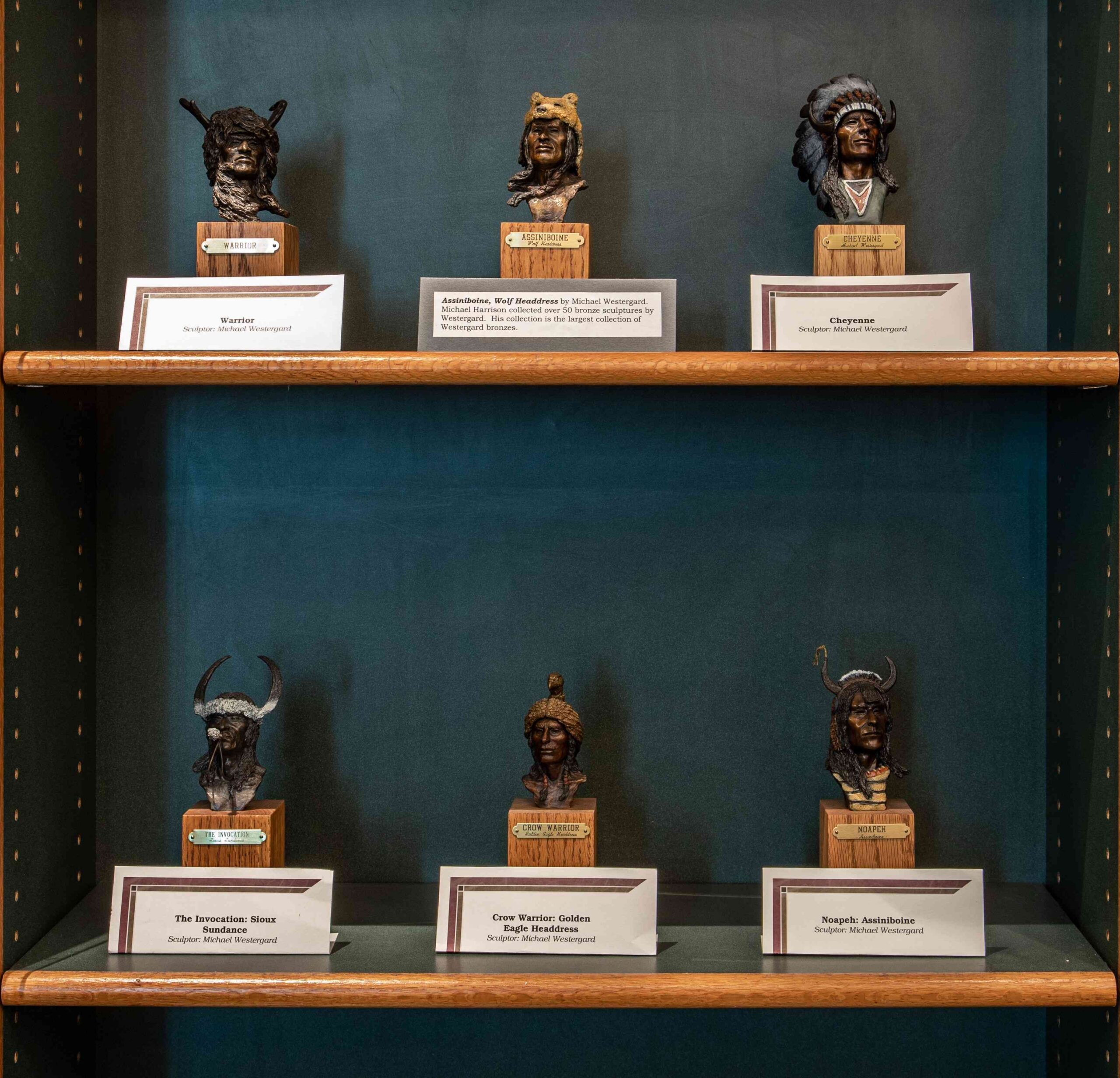Various sculptures of Native American figures lined up on two shelves.