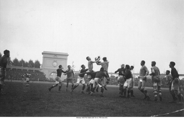 A black and white photograph of a rugby game. Two men struggle midair to catch the ball.