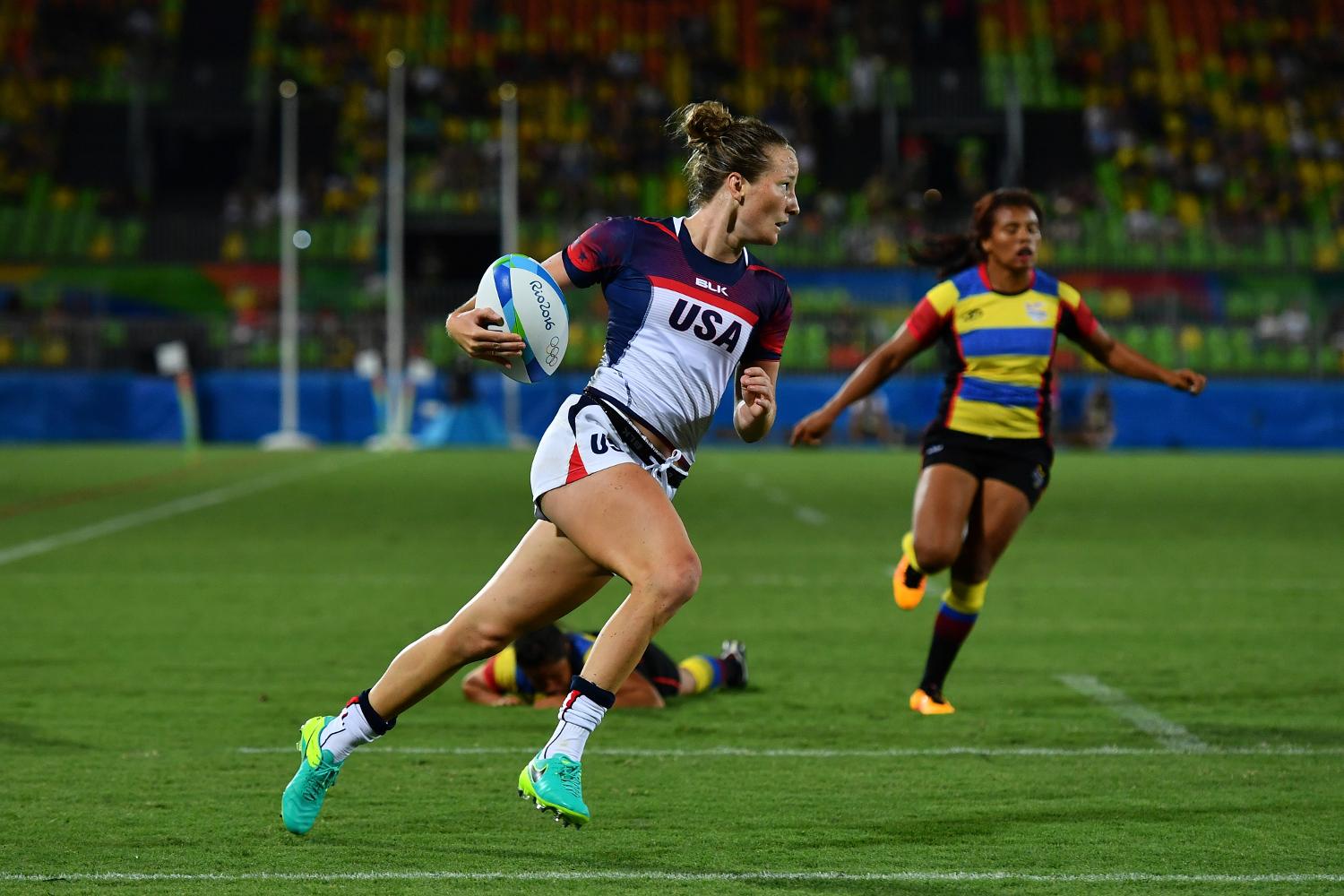 Two women running, one with a rugby ball in hand.