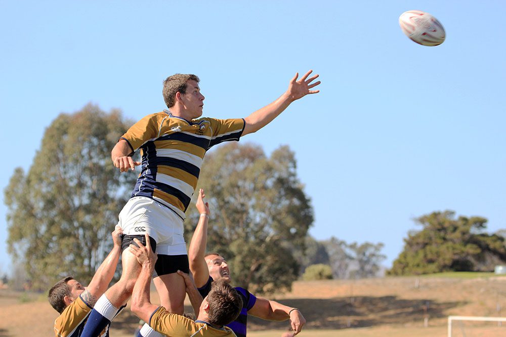 A UC Davis player being raised into the air by his teammates in order to catch the rugby ball.