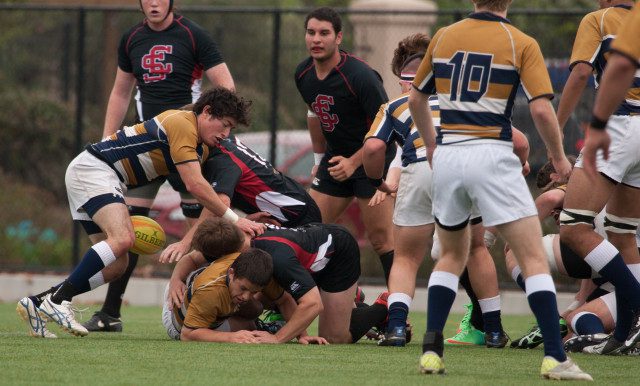 A group of men tackling each other for the rugby ball.