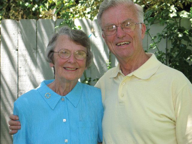 An older man and woman smiling at the camera outside on a sunny day.