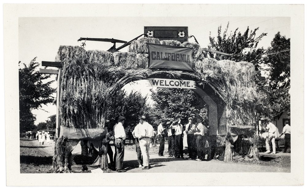 A black and white photograph of a large arch made of wood and straw reading, "California. Welcome."