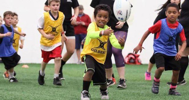 Small children playing ruby. A child in the center reaches to catch the ball.