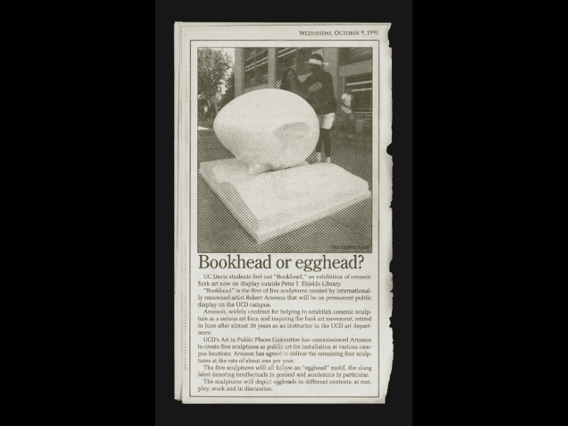 Newspaper clipping including a photo of Bookhead sculpture, with two students standing by it. One of them is blindfolded.