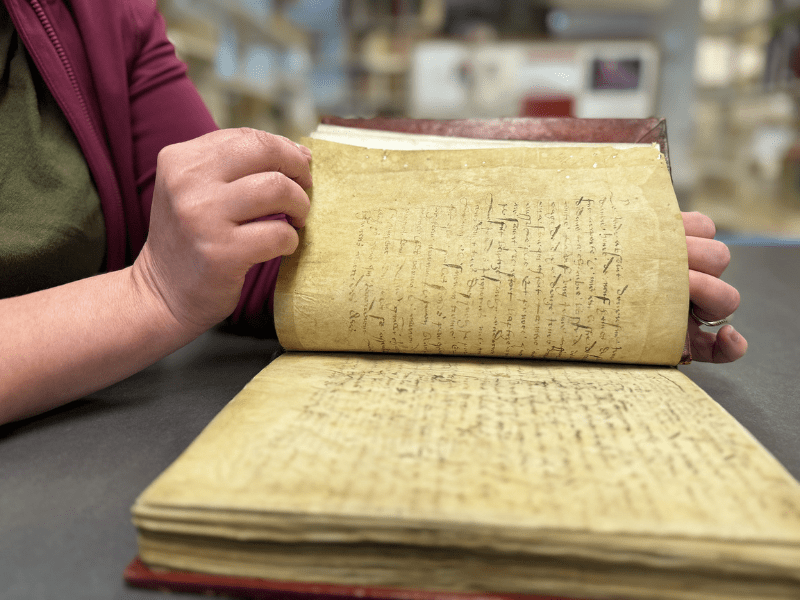A very old book with someone opening it. The pages are deeply yellowed with tiny holes dotting the edges.