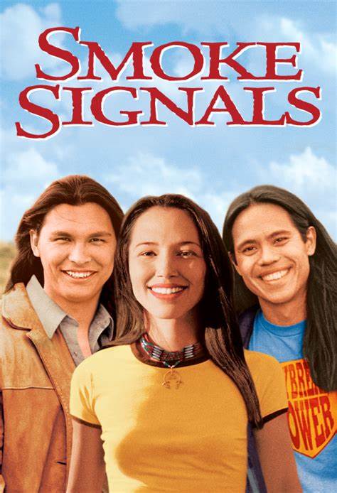 Smoke Signals film poster showing three young Indigenous adults standing together outdoors and smiling. The title “Smoke Signals” appears in large red lettering at the top.