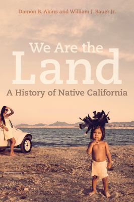 We Are the Land book cover showing two children standing near a shoreline under a muted sky, with layered white title text reading “We Are the Land.”