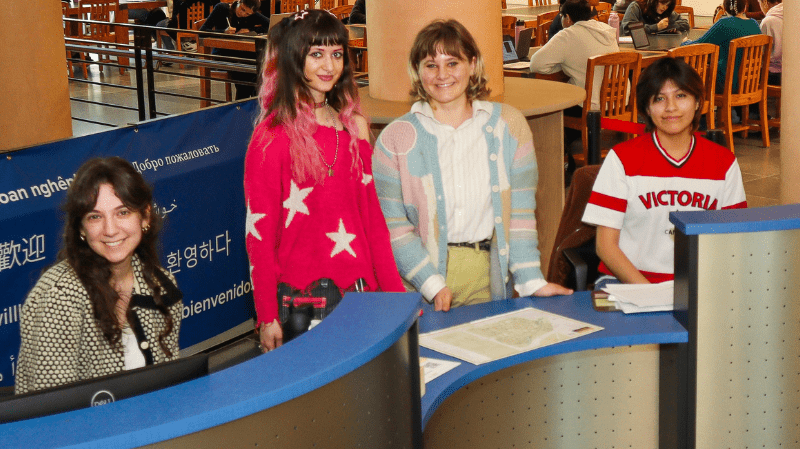 Students standing behind a modern steel welcome desk in the lobby at Shields Library.