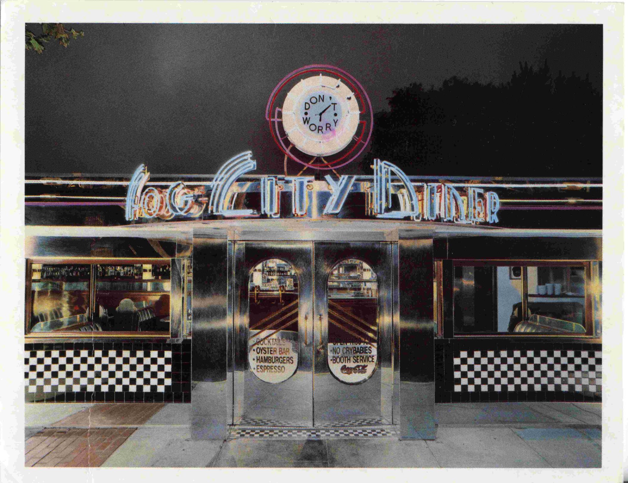 Postcard from 1990 of the Fog City Diner in San Francisco at night. The doors and a light-up "Fog City Diner" sign are in the center foreground