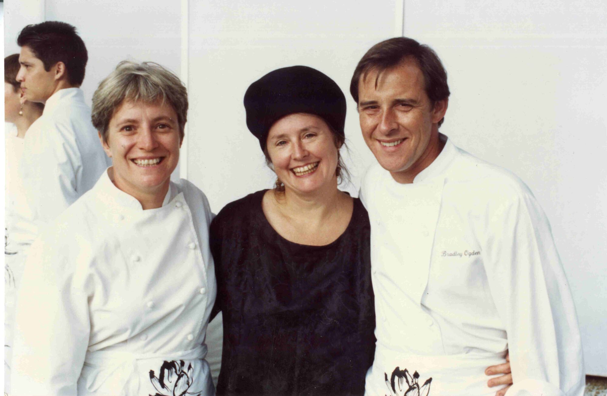 Photograph of 3 chefs with their arms around each other. From left to right: Cindy Pawlcyn, Alice Waters, and Brad Ogden.