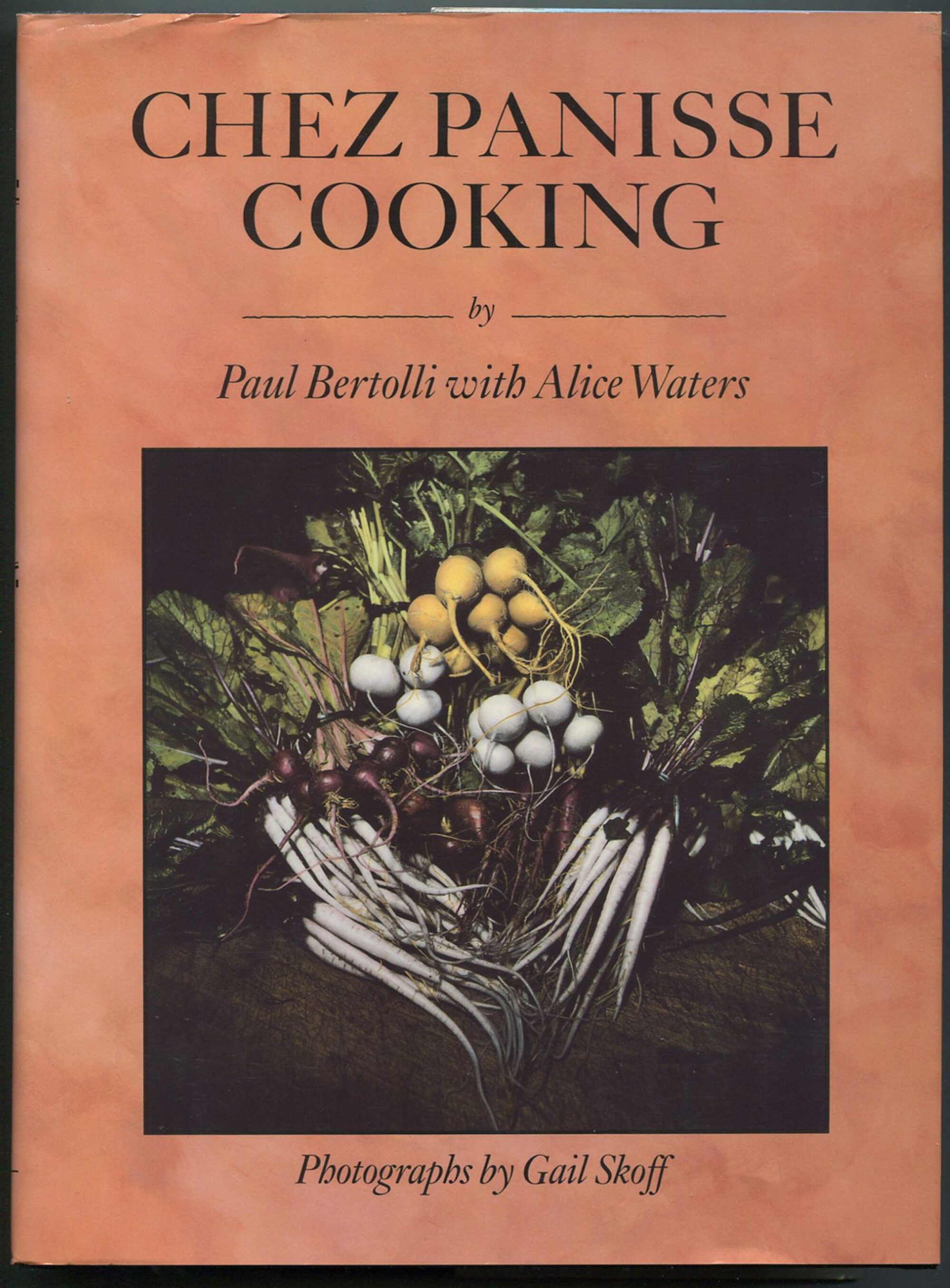 The book title "Chez Panisse Cooking" by Paul Bertolli with Alice Waters appears above a photograph of various root vegetables. Text below the photo reads "Photographs by Gail Skoff" in italicized serif font.