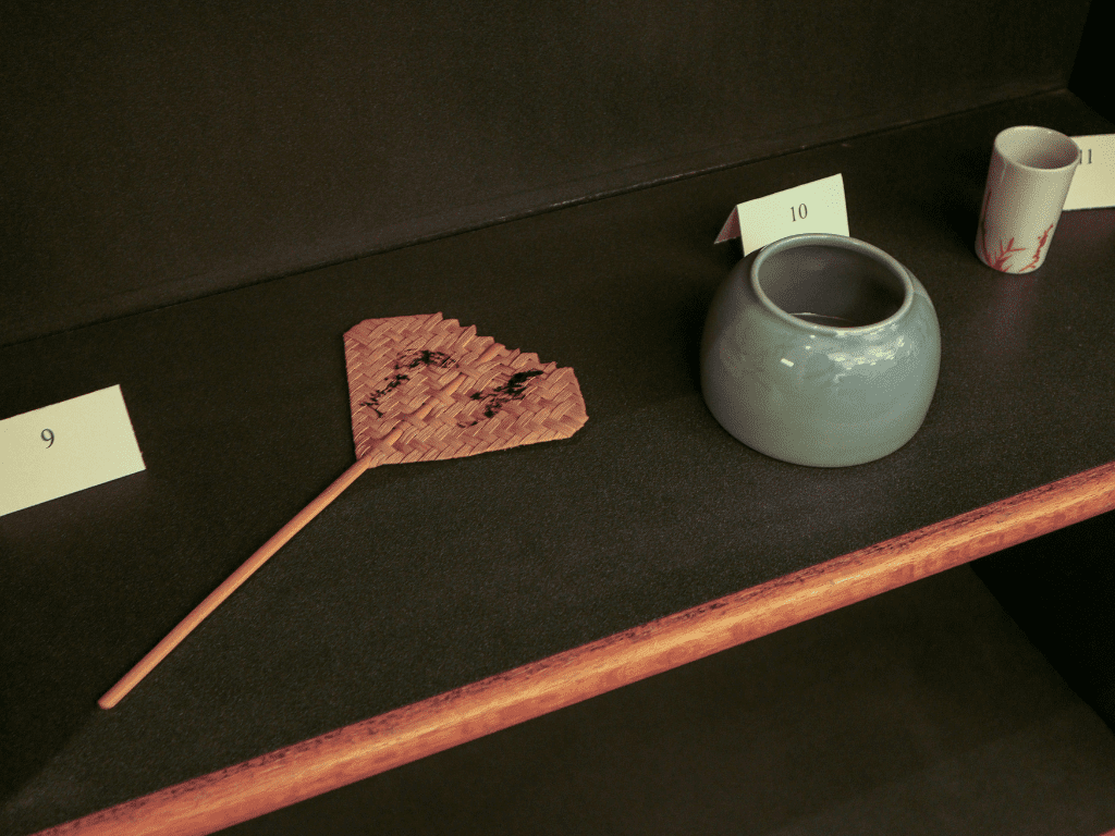Left to right: Woven bamboo fan, green ceramic pot, small white ceramic holder with red inscription