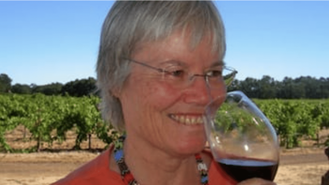 An older woman lifts a glass of red wine to drink.