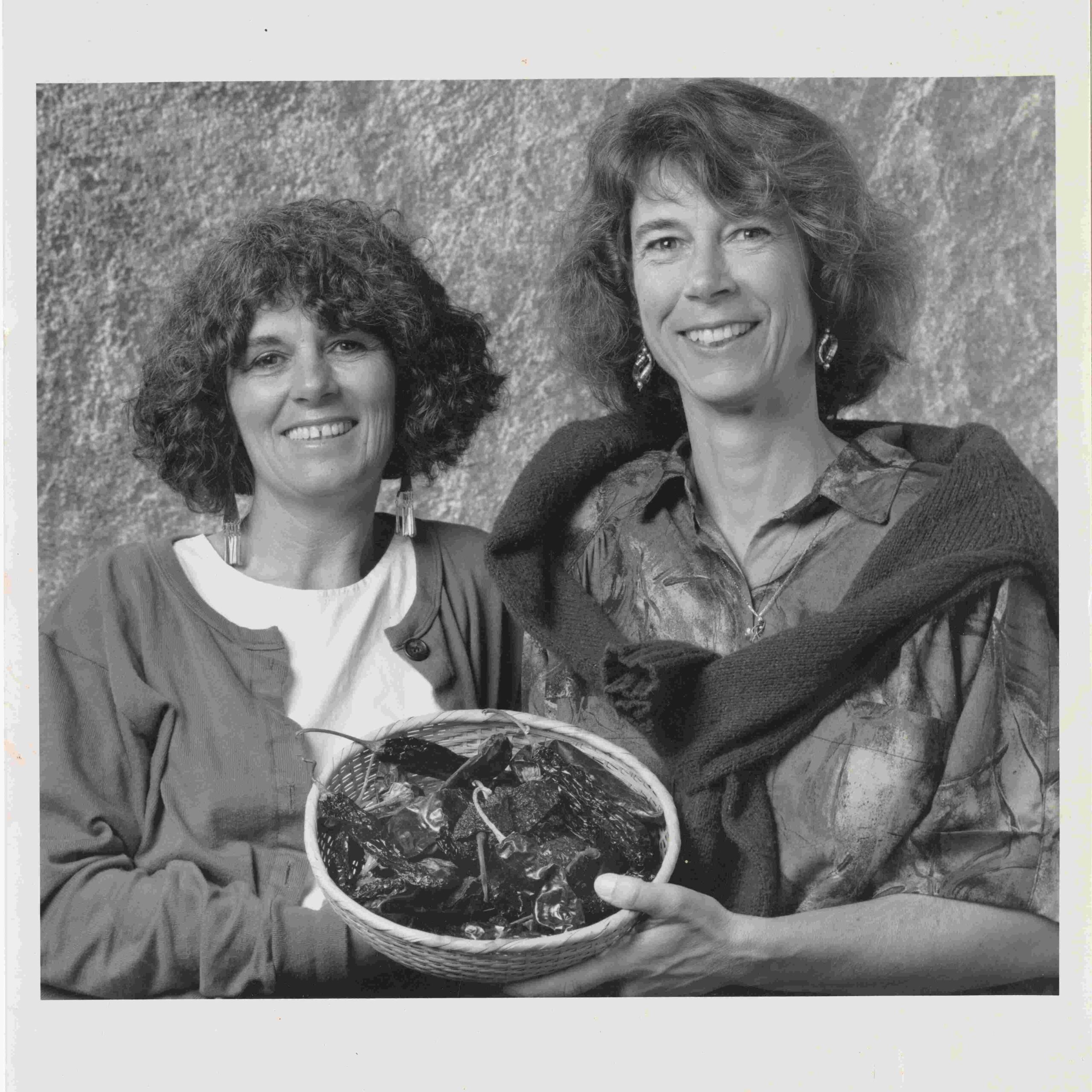 Two women in the center smiling and holding a basket of vegetables