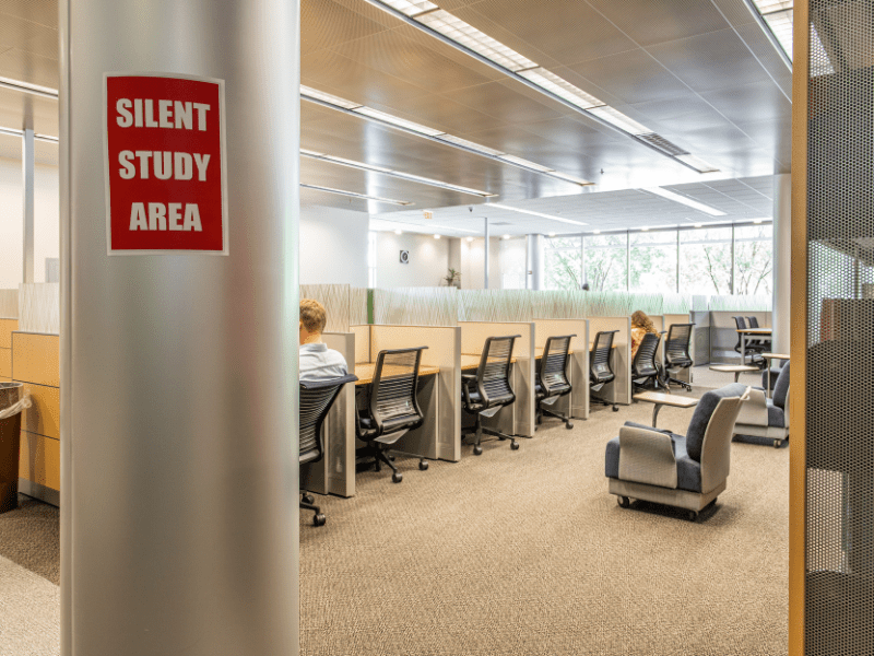 Row of cubicles with a couple of student studying. A sign on a post reads Silent Study Area.