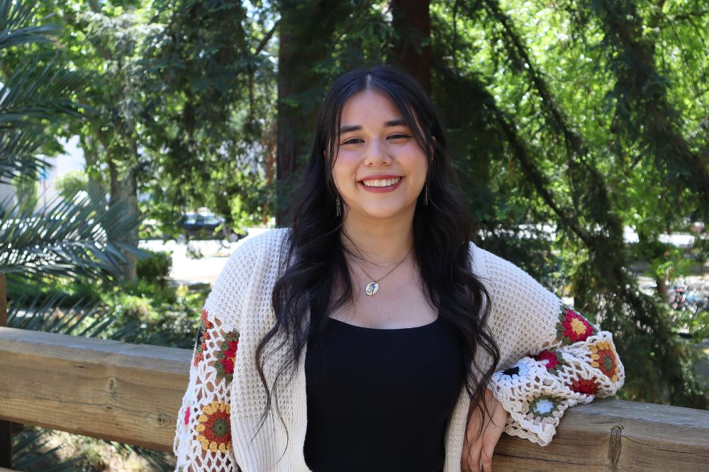 Portrait of Mariana Perez Sierra wearing a white knit sweater with colorful design on the sleeves over a black shirt